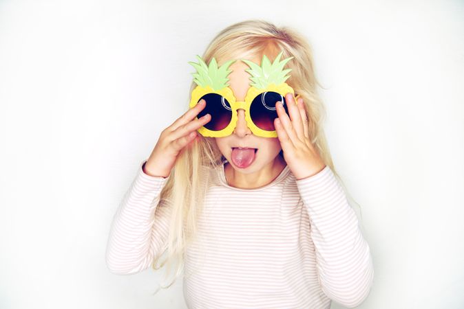 Blonde girl having fun adjusting her big pineapple sunglasses