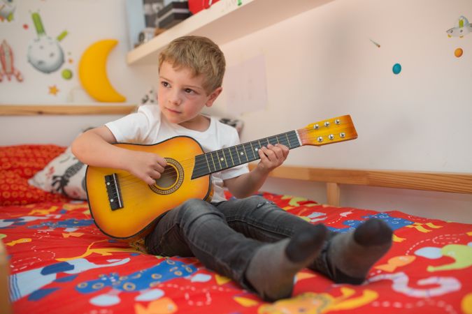 Young blonde boy playing toy guitar
