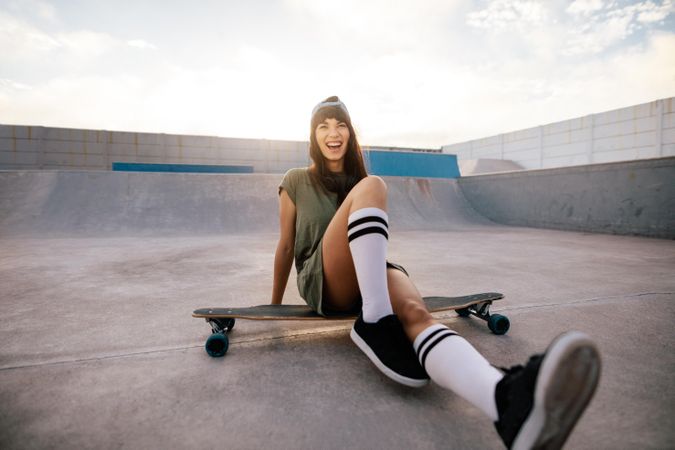 Female skater having fun at skate park siting on skateboard