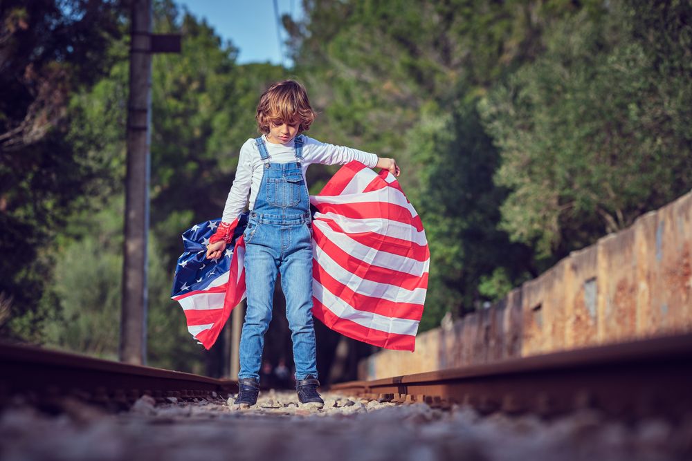 Preteen boy with waving American national flag standing on railr