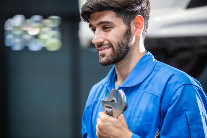 Smiling male mechanic holding wrench at auto garage