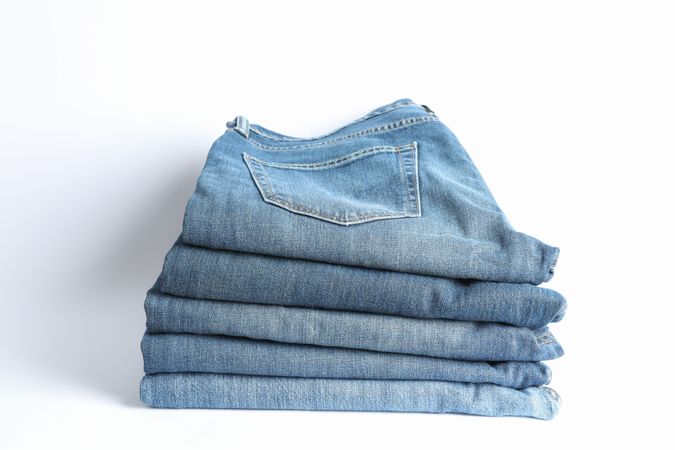 Stack of jeans pants on light background, space for text