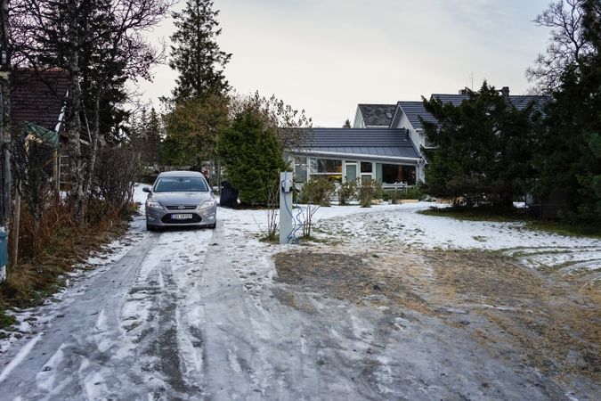 Gray electric car on snowy yard near country house among beautiful garden in winter