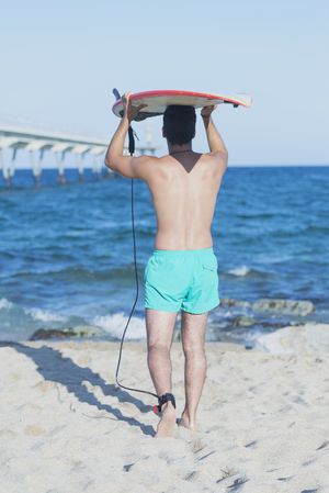 Full body shot of male surfer looking out to the ocean with board on head