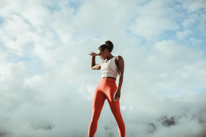 Slender woman taking break from workout and looking away against cloudy sky outdoors