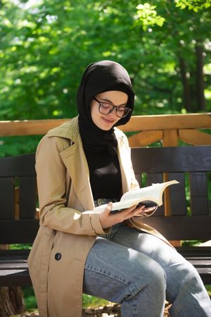 Woman in headscarf calmly reading in a wooded park