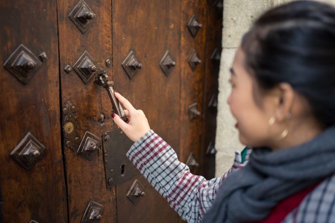Curious female traveler in casual wear clattering in ancient door at city street