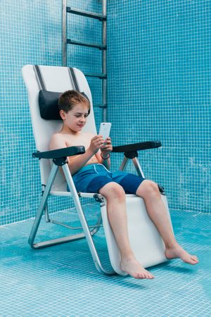 Boy with smartphone sitting on bottom of empty pool