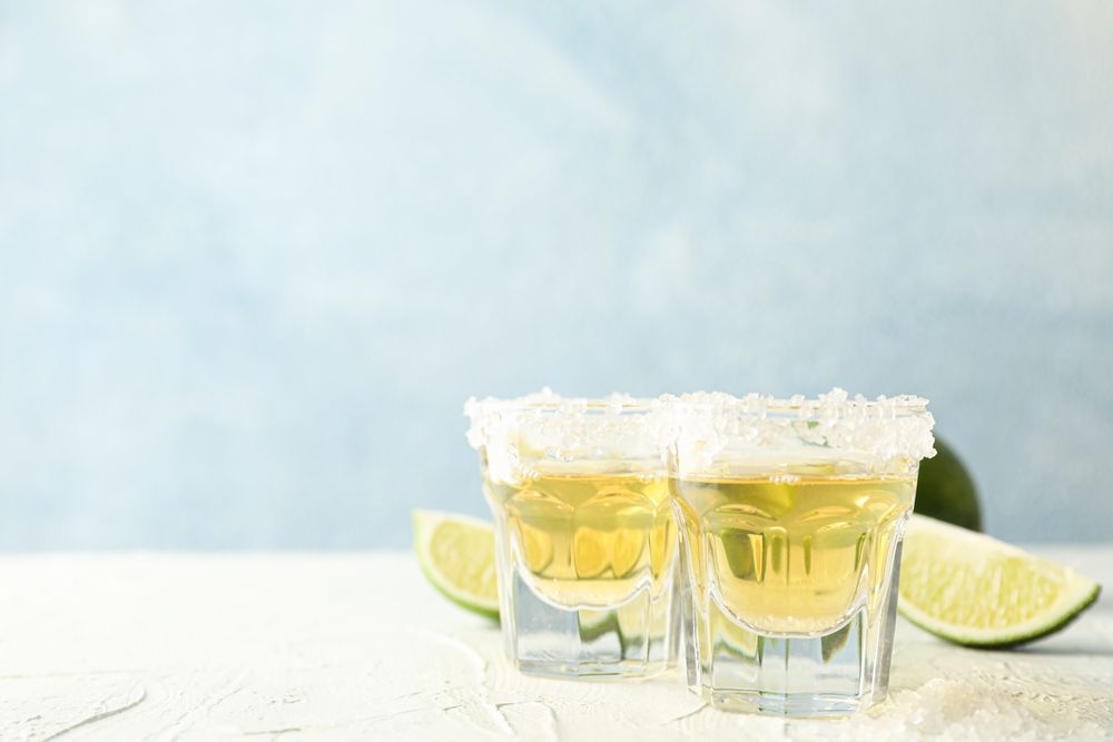 Tequila shots with salt and lime slices on light background