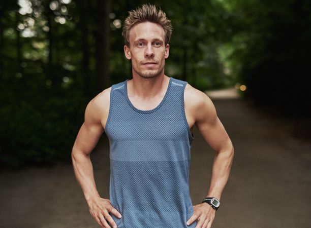 Confident man in sport clothing standing on running trail in the forest