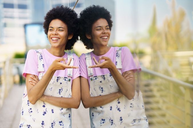 Joking female in floral overalls leaning on window outside