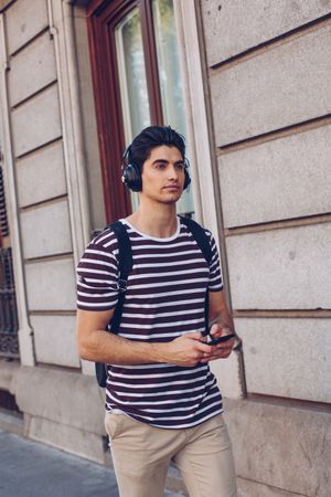 Young man with headphones and smartphone walking outdoors