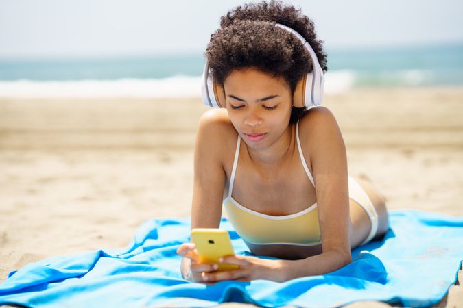 Female with curly hair on beach towel reading phone