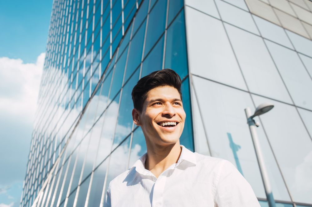 Smiling young man in sunlight under skyscraper