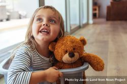 Adorable young girl sitting in a laundry basket with her teddy bear bGNXl4