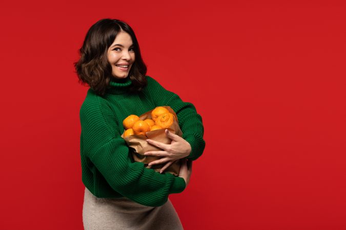 Woman in green sweater holding paper bag filled with tangerines