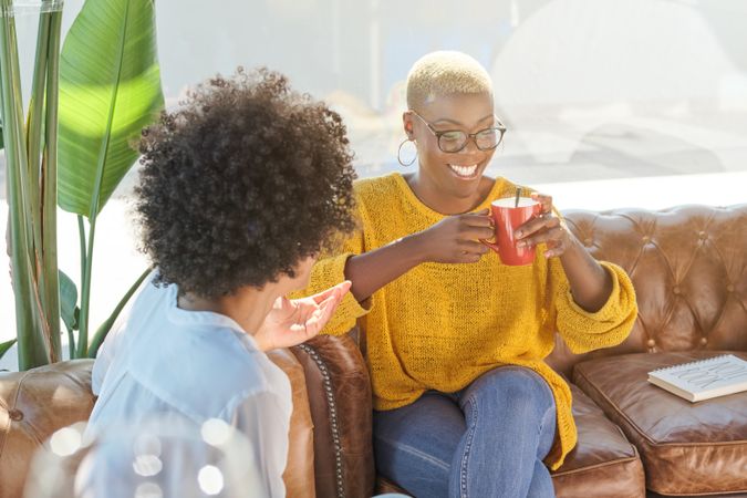 Cheerful Black women drinking hot tea and talking at home