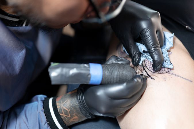 A tattoo artist is tattooing a snake and a rose on a woman's leg. Close up.
