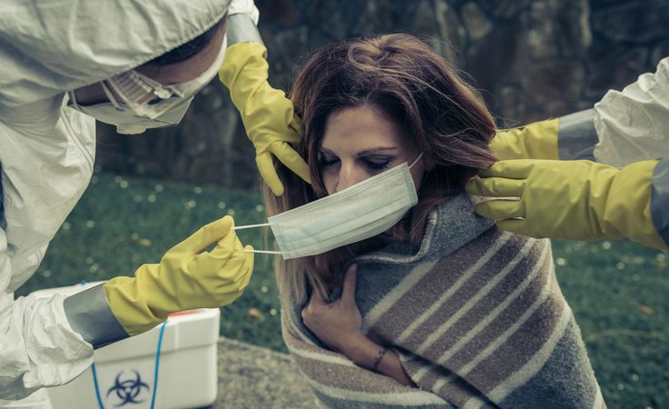 People in bacteriological protective suits putting a mask on woman