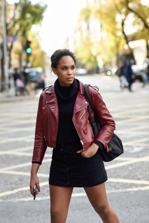 Cosmopolitan woman with handbag on crosswalk holding mobile phone on nice day