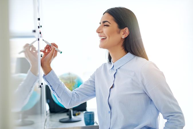 Smiling female entrepreneur working off a dry erase board in bright office