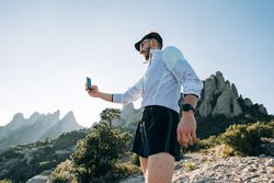 Man in athletic gear taking picture with phone on a hill
