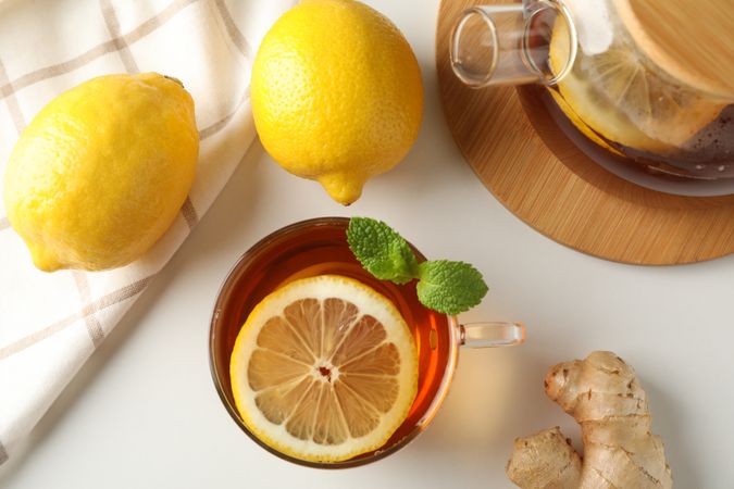 Cup of tea, mint, lemon, tea pot and towel on blank background, top view