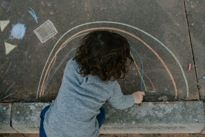 Above shot of child drawing rainbow on the cement