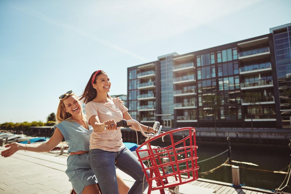Two happy women riding a bicycle along the river walk