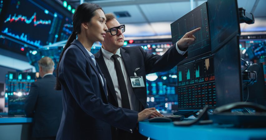 Financial Analysts Using a Computer with Multi-Monitor Workstation with Real-Time Graphs, Financial Reports and Market Charts.