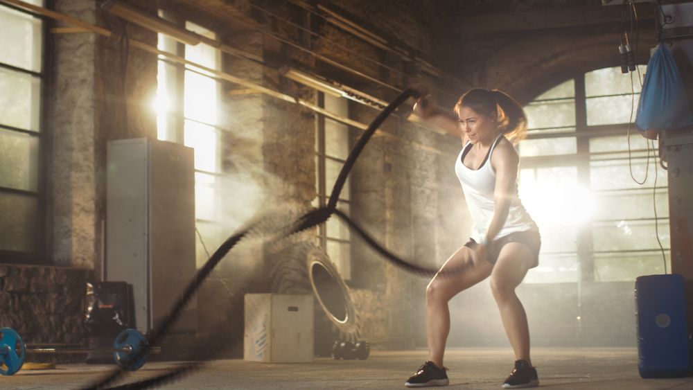 Athletic Female in a Gym Exercises with Battle Ropes During Her Cross Fitness Workout  High-Intensity Interval Training.