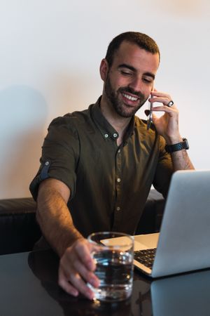 Cheerful man talking on smartphone near laptop