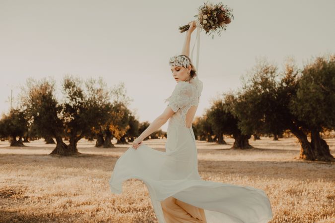 Content woman in dress with open back raising hands with flower bouquet