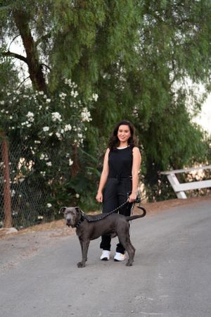 Full length portrait of a woman in casual attire standing in the street with her dog on a leash