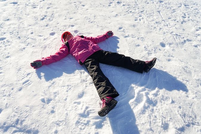 Child in pink snow suit lying in the snow making snow angel