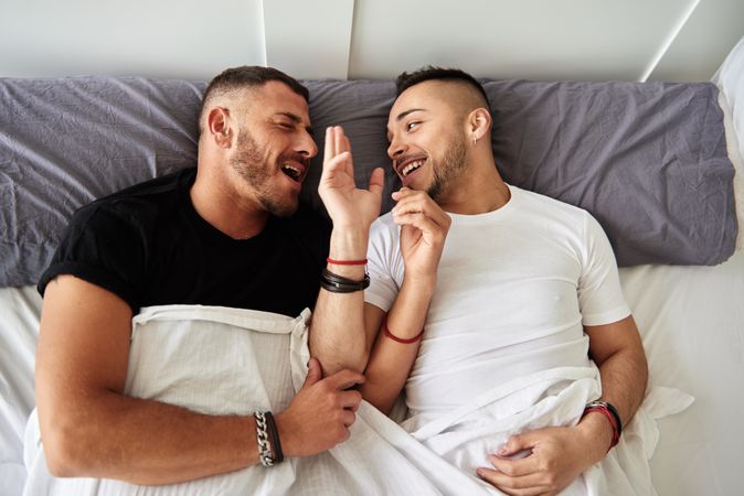 Smiling gay couple hugging on bed