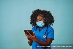 Portrait of serious Black medical professional in face mask dressed in scrubs with tablet bYRnX0