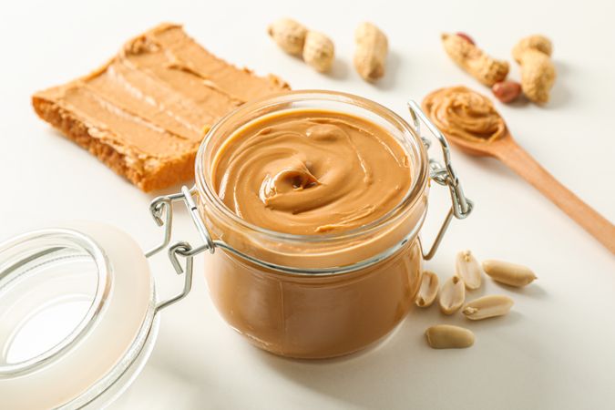 Composition with peanut butter sandwich, glass jar, peanut and spoon on light background, space for text and closeup