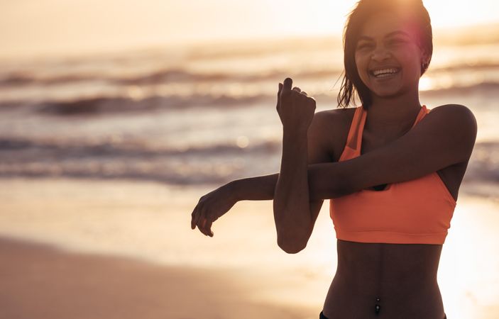 Smiling woman stretching arms at the sea shore