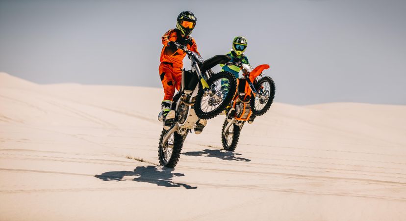 Two motocross riders doing wheelie together over sand dunes