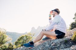 Male athlete adjusting hat on rocks he’s sitting on