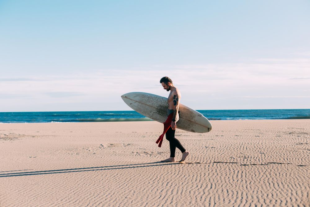 Man in wetsuit walking along the coast with surfboard
