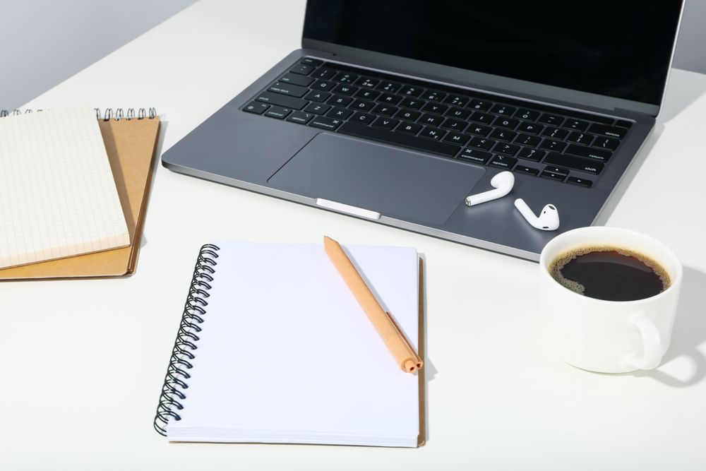 Table with open laptop, earbuds, coffee, and blank notebooks
