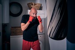 Man training boxing in the laundry room at home with a bag