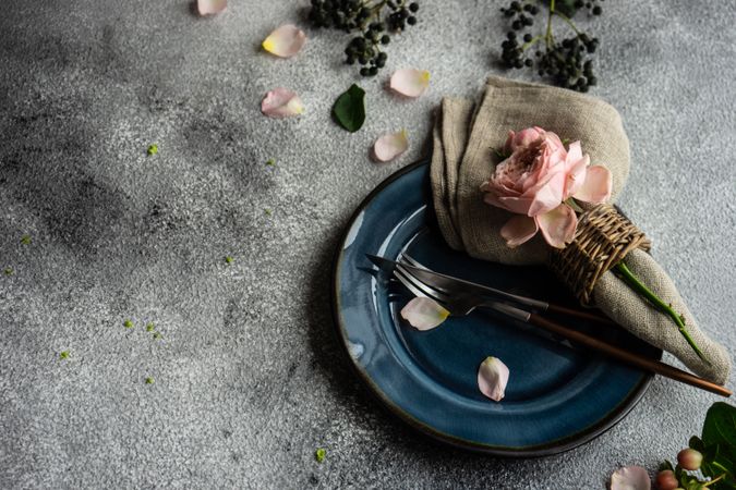 Delicate pink flowers on grey napkin and blue plate with silverware