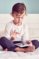 Serious boy playing game on tablet in bedroom