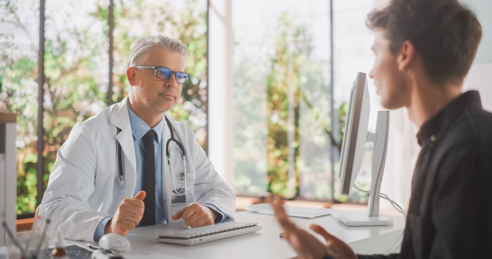 Doctor is Having a Conversation with a Young Patient, Speaking with Him During Consultation in a Health Clinic