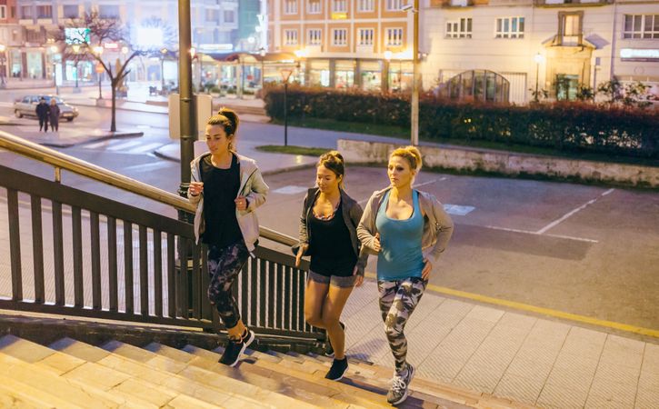 Fit female friends training running up stairs in city at night