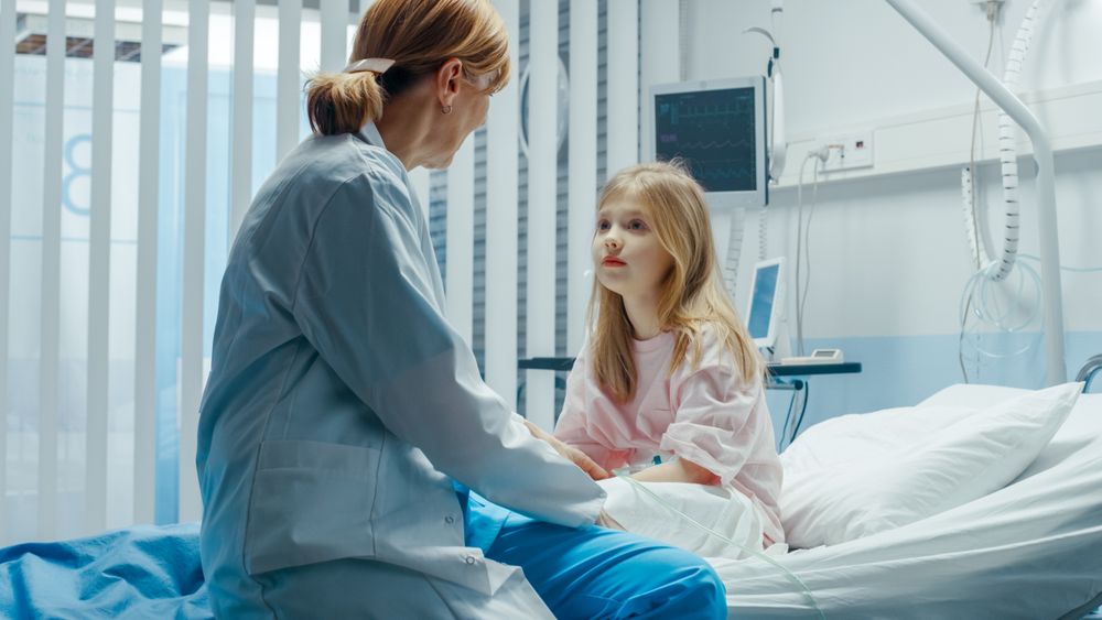 Recovering Little Girl Sits on a Hospital Bed and Talks with Friendly Woman Doctor