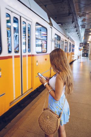 Long haired woman with smartphone standing in front of subway car